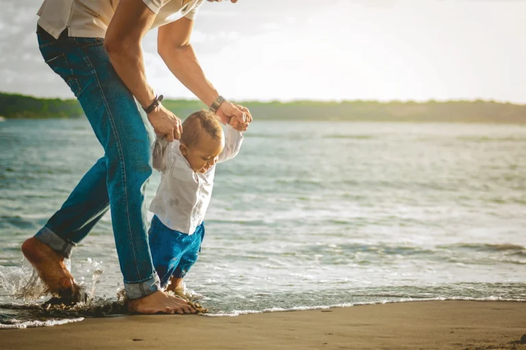 Baby an den Händen eines Masses Strand Laufübungen